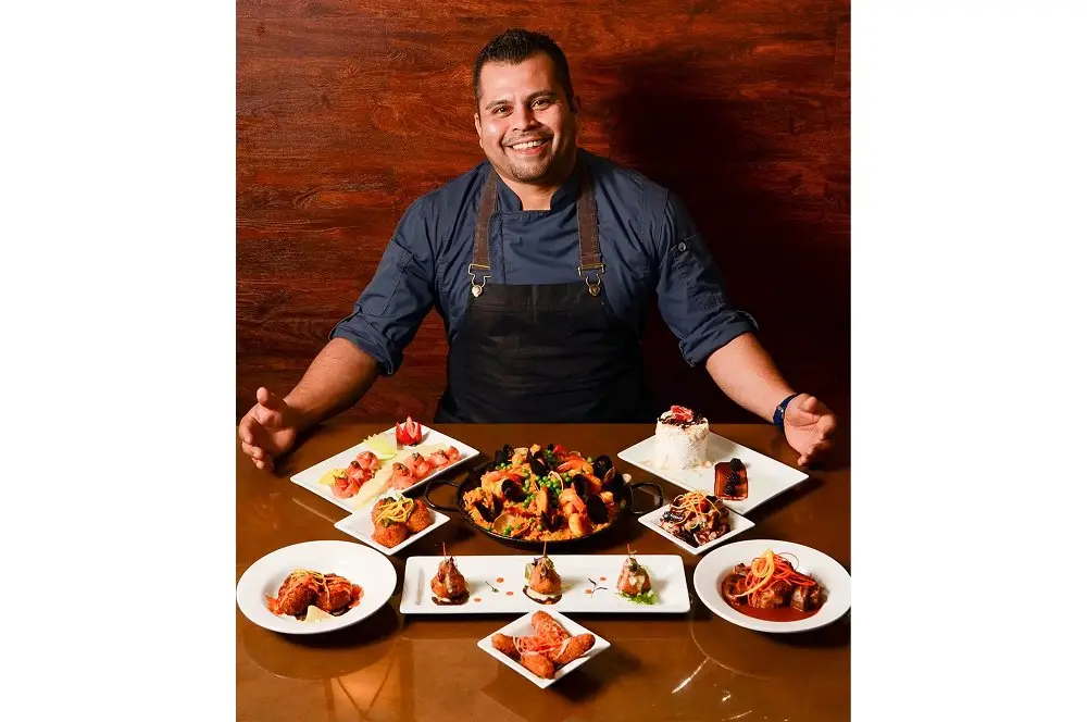 A man in an apron sits at a table filled with various dishes, ready to enjoy a meal.
