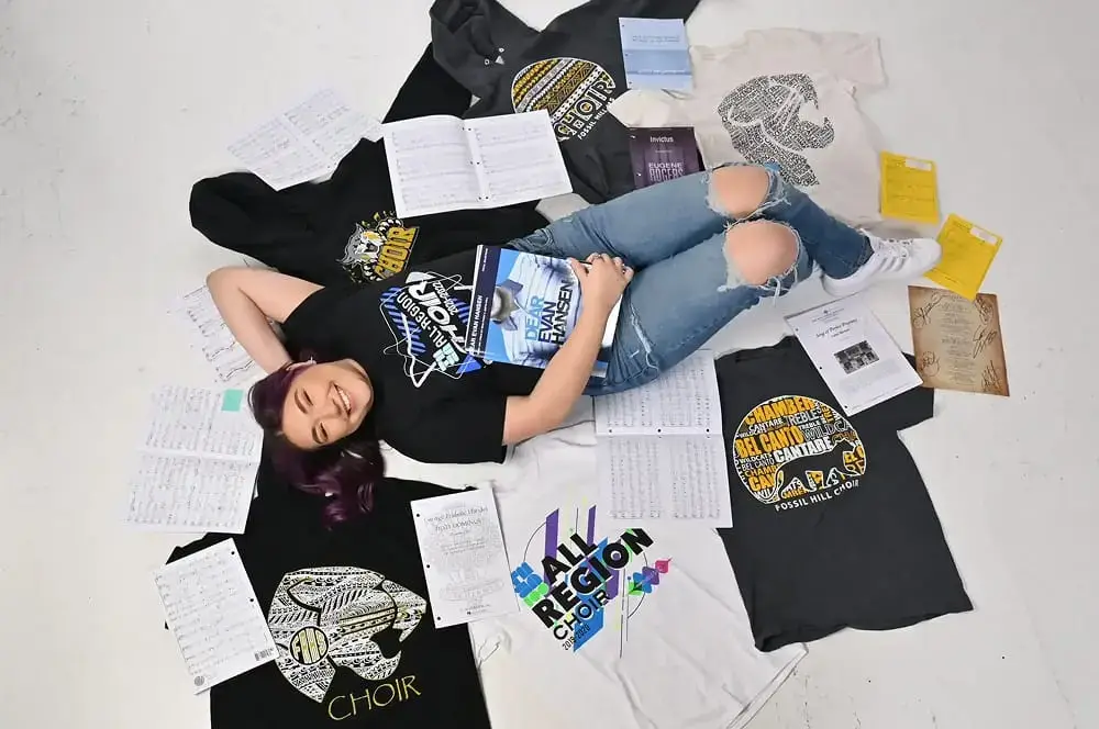 A woman lies on the floor, surrounded by scattered books and colorful t-shirts, creating a cozy reading space.